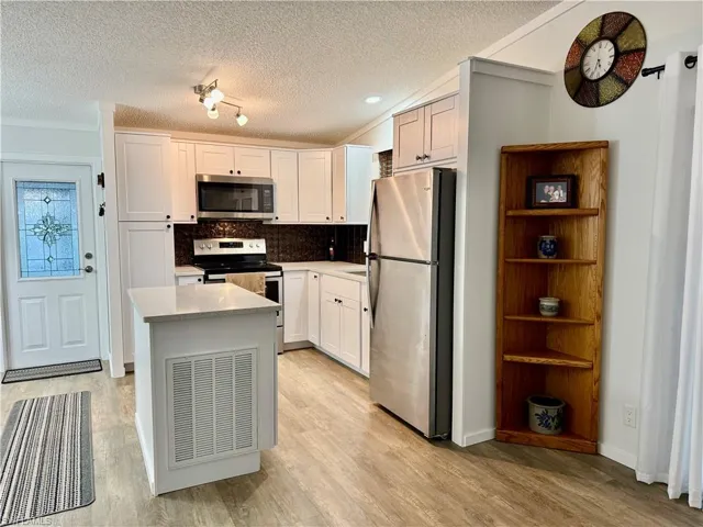 Kitchen featuring backsplash, track lighting, white cabinets, a textured ceiling, and appliances with stainless steel finishes