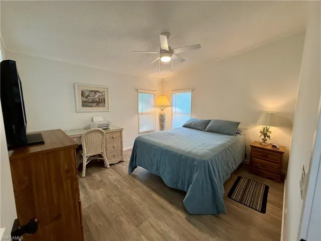 Bedroom with a textured ceiling, hardwood / wood-style flooring, ceiling fan, and ornamental molding