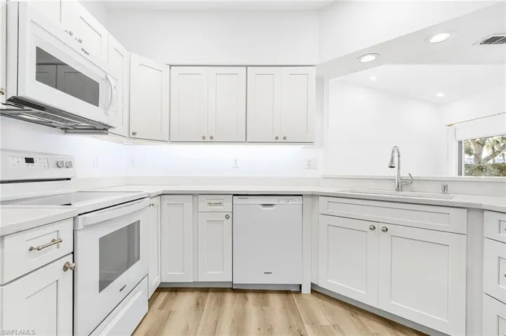 Kitchen featuring white appliances, white cabinets, recessed lighting, light wood-type flooring, and light stone counters