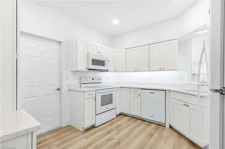 Kitchen featuring white appliances, white cabinetry, light wood-style flooring, and recessed lighting