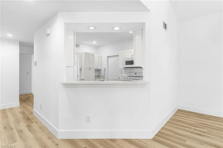 Kitchen with white cabinetry, light wood-style flooring, white appliances, light stone counters, and recessed lighting