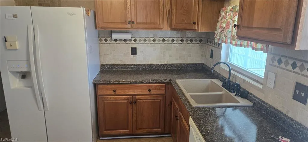 Kitchen with white appliances, decorative backsplash, and brown cabinetry
