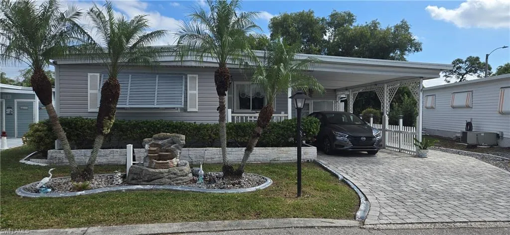 Manufactured / mobile home featuring a carport, decorative driveway, covered porch, and a front yard