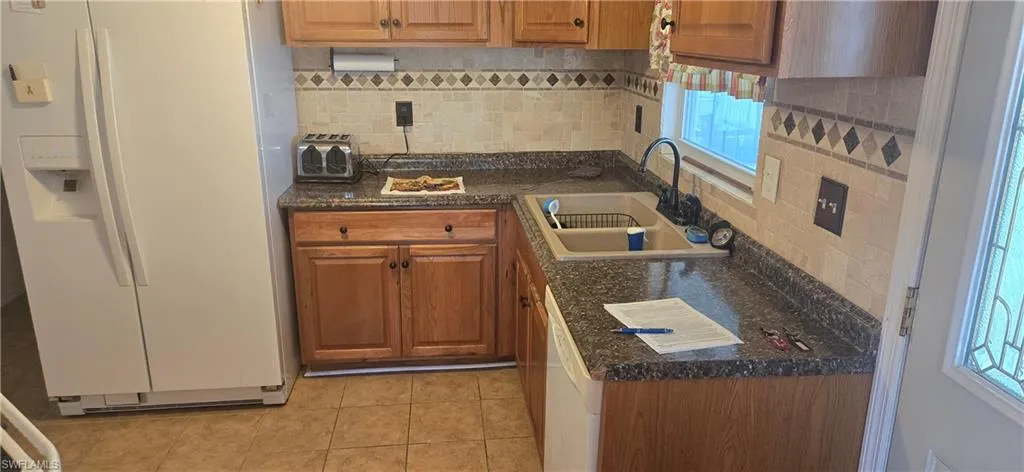 Kitchen featuring white appliances, backsplash, light tile patterned floors, and brown cabinetry