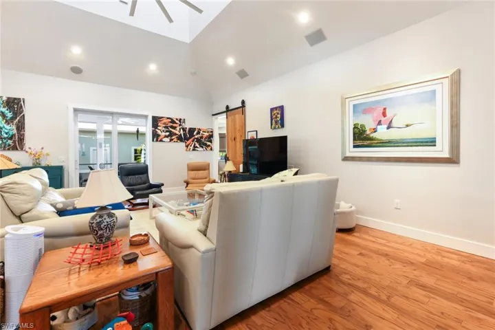 Living area with a barn door, lofted ceiling, wood finished floors, a ceiling fan, and baseboards