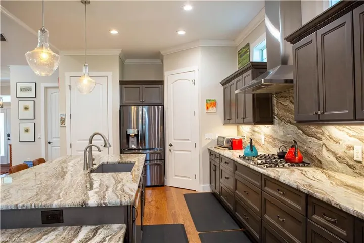 Kitchen featuring stainless steel appliances, a sink, dark brown cabinets, wall chimney exhaust hood, and light wood finished floors