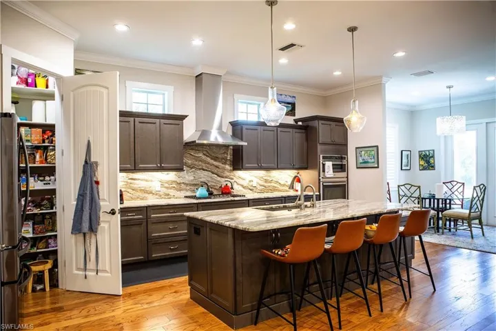 Kitchen with wall chimney exhaust hood, appliances with stainless steel finishes, dark brown cabinets, a sink, and hardwood / wood-style flooring