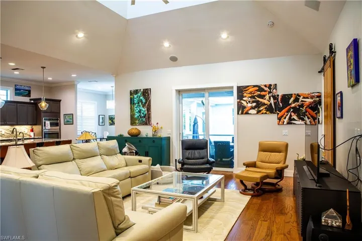 Living area with wood finished floors, lofted ceiling, a barn door, recessed lighting, and ornamental molding