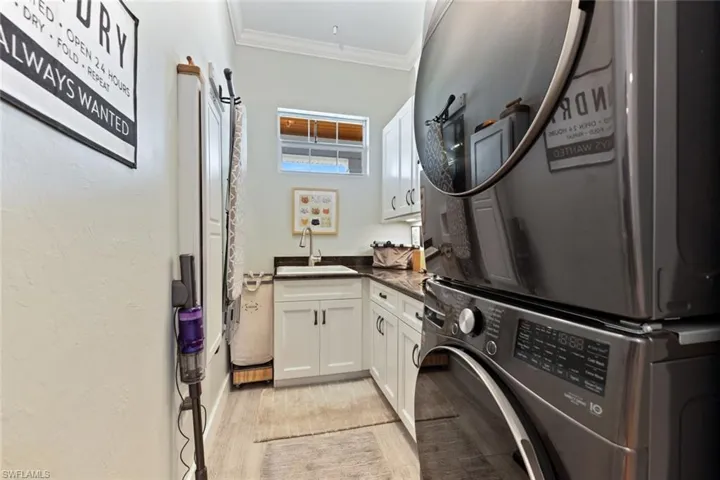 Laundry area with stacked washing machine and dryer, cabinet space, light wood-style floors, and ornamental molding