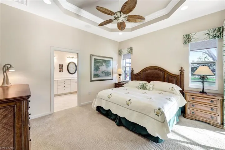 Bedroom featuring crown molding, a tray ceiling, light carpet, and ensuite bathroom