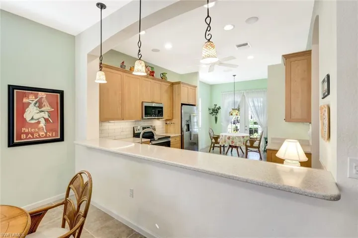 Kitchen with appliances with stainless steel finishes, pendant lighting, tasteful backsplash, kitchen peninsula, and light brown cabinets