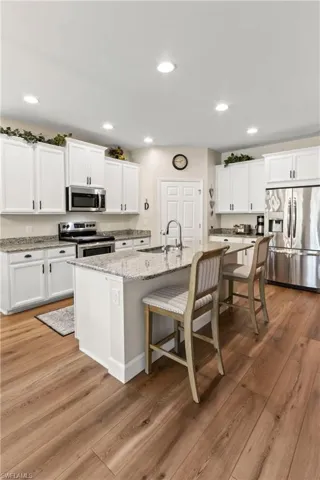 Kitchen featuring white cabinetry, appliances with stainless steel finishes, light wood-style flooring, recessed lighting, and light stone countertops