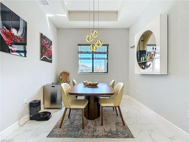 Dining space with light marble finish floors and a tray ceiling