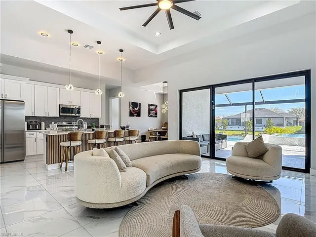 Living room featuring a ceiling fan, recessed lighting, light marble finish flooring, and a raised ceiling