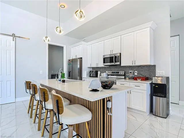 Kitchen featuring a barn door, white cabinetry, a kitchen bar, stainless steel appliances, and a center island with sink