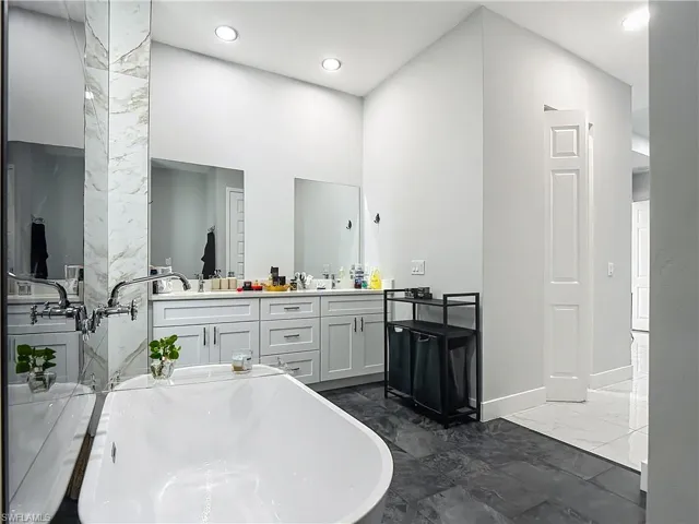 Full bathroom featuring double vanity, a freestanding tub, dark marble finish flooring, a high ceiling, and recessed lighting