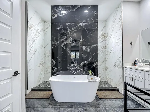 Bathroom with stone wall, tile walls, a freestanding bath, vanity, and a marble finish shower