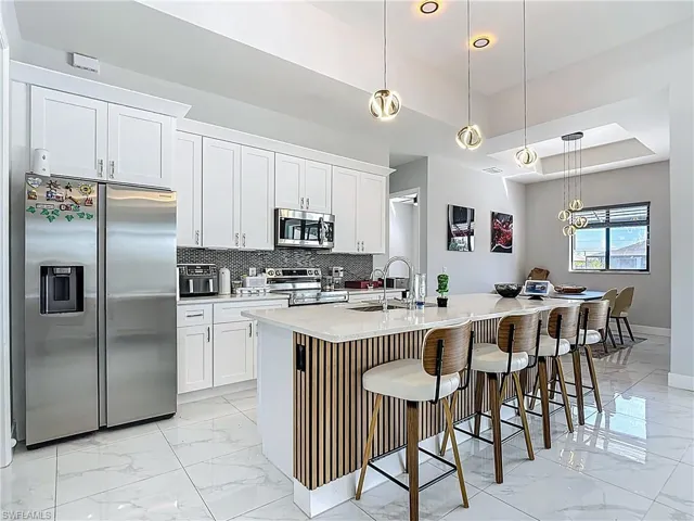 Kitchen with a breakfast bar area, pendant lighting, stainless steel appliances, a kitchen island with sink, and a tray ceiling