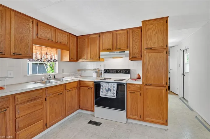 Kitchen featuring white electric range oven, light countertops, under cabinet range hood, and backsplash