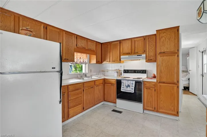 Kitchen featuring white appliances, light countertops, tasteful backsplash, brown cabinets, and under cabinet range hood