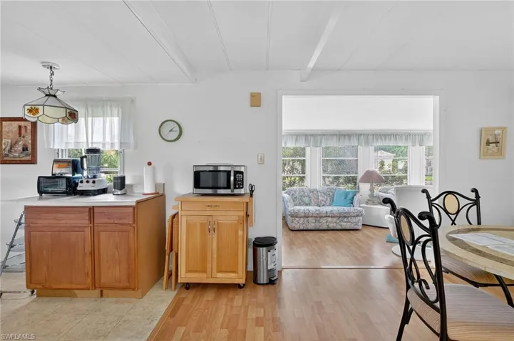 Kitchen featuring light wood-type flooring, stainless steel microwave, light countertops, beamed ceiling, and hanging light fixtures