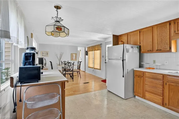 Kitchen with freestanding refrigerator, brown cabinets, light countertops, tasteful backsplash, and hanging light fixtures