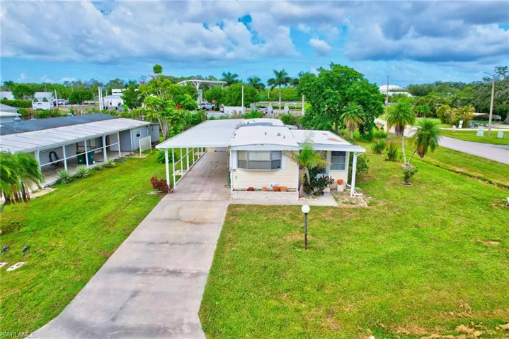 View of front of property featuring concrete driveway, a front yard, a carport, and view of scattered trees