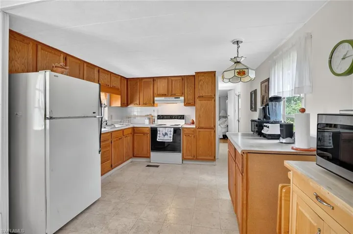 Kitchen featuring white appliances, light countertops, hanging light fixtures, decorative backsplash, and brown cabinets