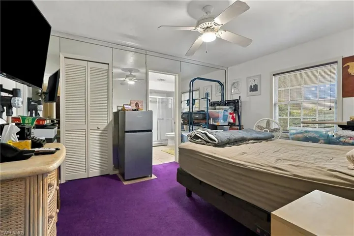 Room featuring wall-to-wall mirrored closet doors, a multi-pane window with horizontal blinds, and a white ceiling fan with integrated lighting