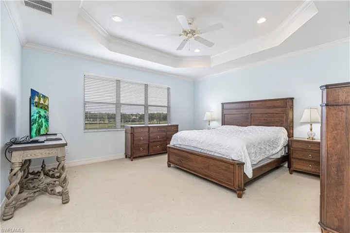 Bedroom with ceiling fan, light carpet, ornamental molding, and a tray ceiling