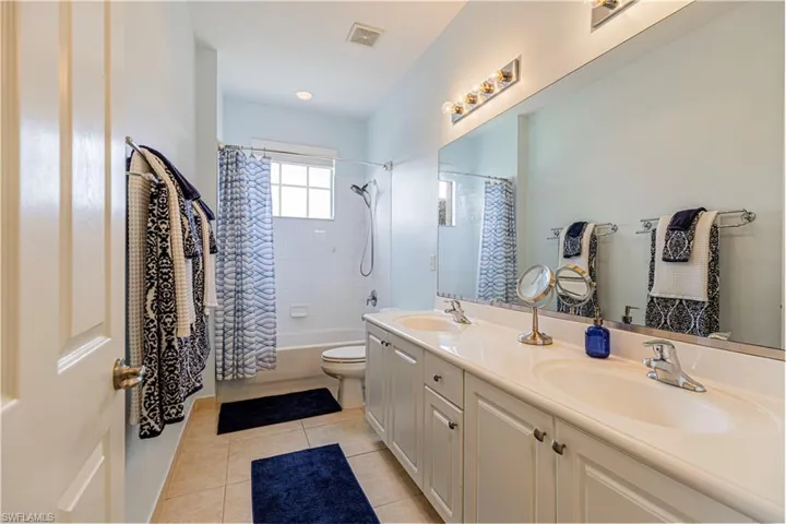 Full bathroom featuring shower / bath combo with shower curtain, toilet, double sink vanity, and tile patterned flooring