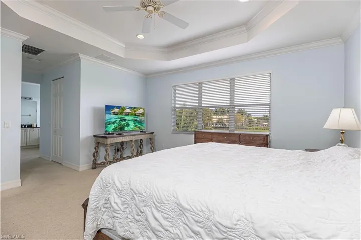 Carpeted bedroom featuring a raised ceiling, ornamental molding, and ceiling fan