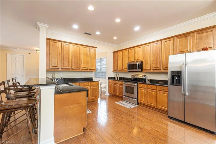 Kitchen featuring crown molding, light wood-type flooring, a breakfast bar area, appliances with stainless steel finishes, and kitchen peninsula