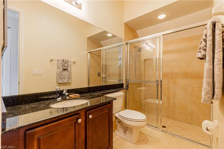 Bathroom featuring a shower with door, vanity, tile patterned floors, and toilet