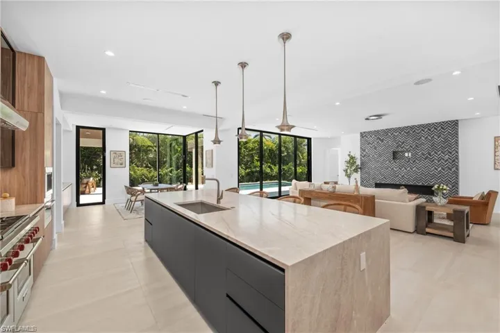 Kitchen with modern cabinets, decorative light fixtures, a large island with sink, an accent wall, and recessed lighting