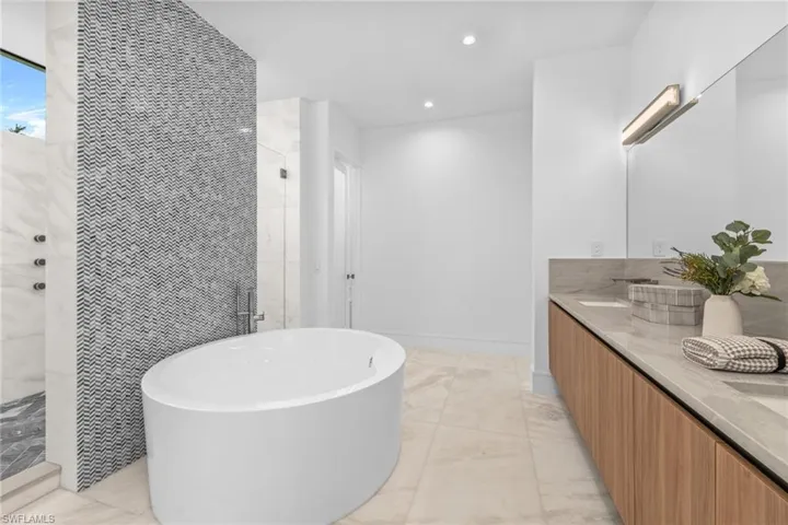 Master Bathroom featuring light marble finish flooring, tiled shower, a freestanding tub, double vanity, and recessed lighting