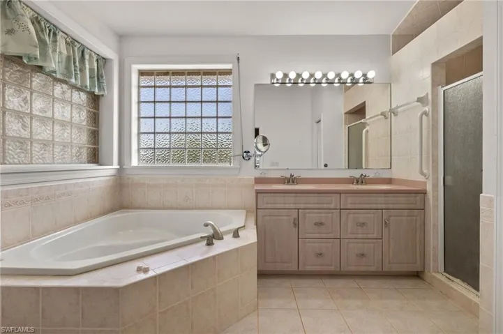 Bathroom featuring shower with separate bathtub, double sink vanity, tile patterned flooring, and tile walls