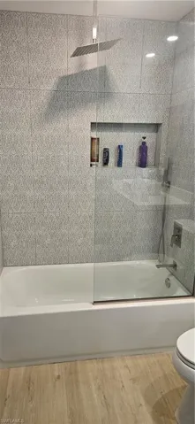 Full bathroom with combined bath / shower with glass door and light wood-style floors
