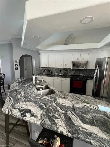 Kitchen featuring dark stone counters, white cabinetry, refrigerator, tasteful backsplash, and ornamental molding