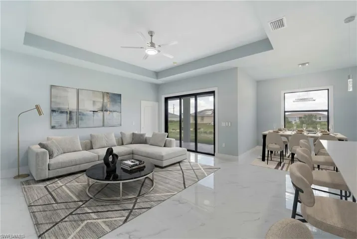Open-concept living space featuring high tray ceilings, polished tile flooring, and sliding glass doors