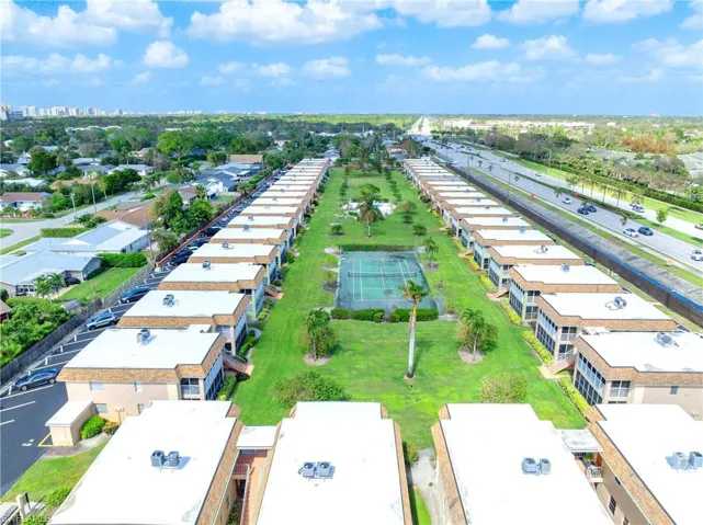Aerial view of the community featuring landscaped green space, tennis courts, swimming pool, and courtyard-style buildings.