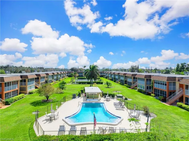 Community pool area surrounded by landscaped green space, sun deck seating, and courtyard-style condominium buildings.