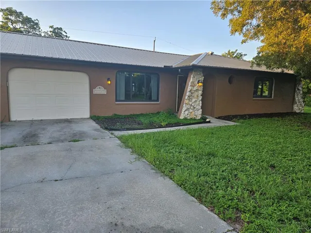 Ranch-style home with stucco siding, driveway, a metal roof, and a front lawn