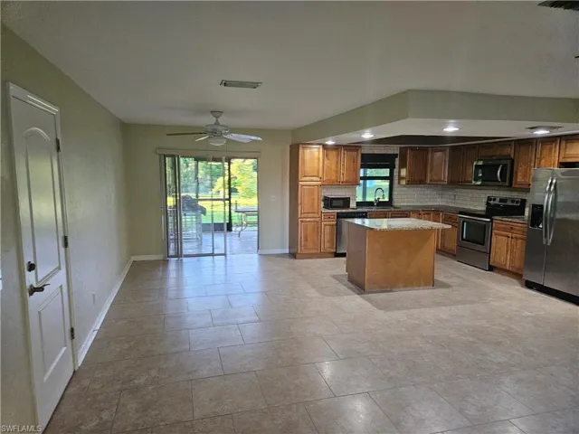 Kitchen featuring appliances with stainless steel finishes, backsplash, light stone countertops, a center island, and a ceiling fan