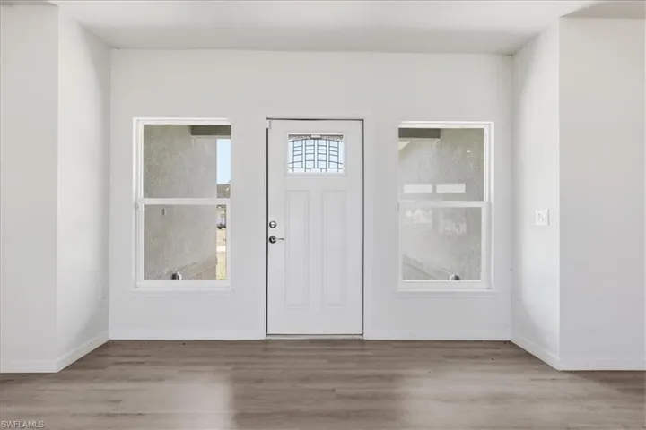 Entryway featuring a white paneled door with decorative glass, two double-hung windows, and wood-finish flooring