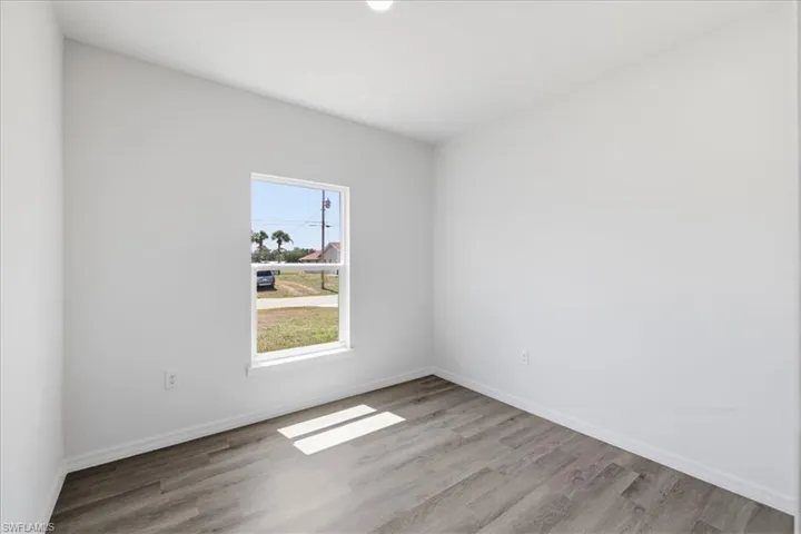 Neutral wall paint, wood-finish flooring, and a single window with white trim