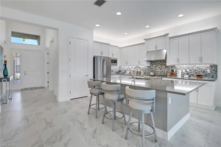 Kitchen with a kitchen bar, appliances with stainless steel finishes, decorative backsplash, an island with sink, and light tile patterned floors