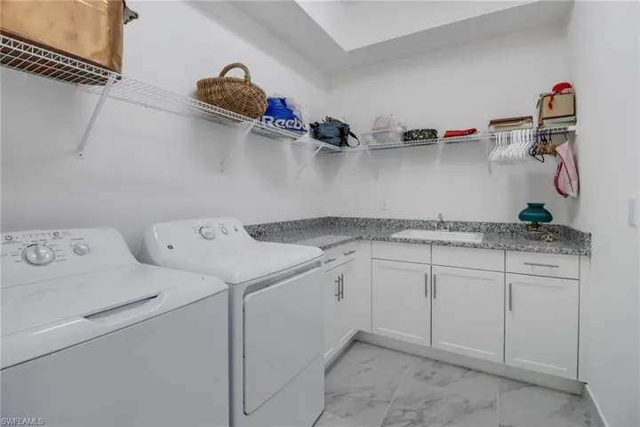 Laundry room with light tile patterned flooring, sink, washing machine and clothes dryer, and cabinets