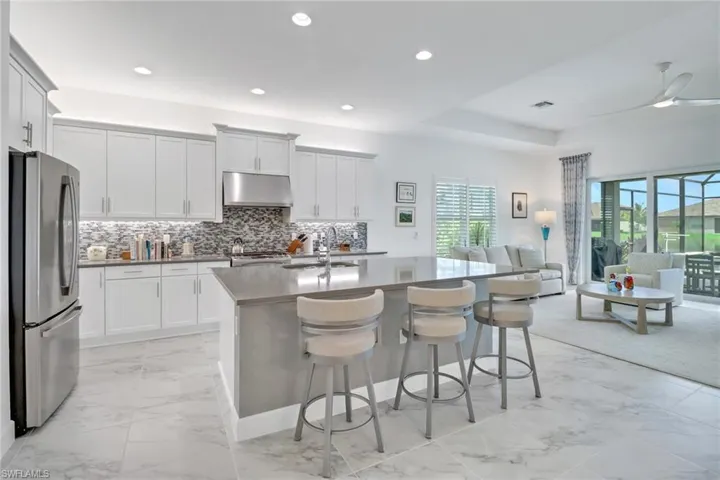 Kitchen featuring decorative backsplash, stainless steel refrigerator, a kitchen island with sink, light tile patterned floors, and ceiling fan