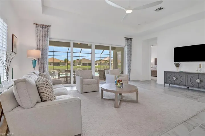 Living room with ceiling fan, a raised ceiling, and light tile patterned floors